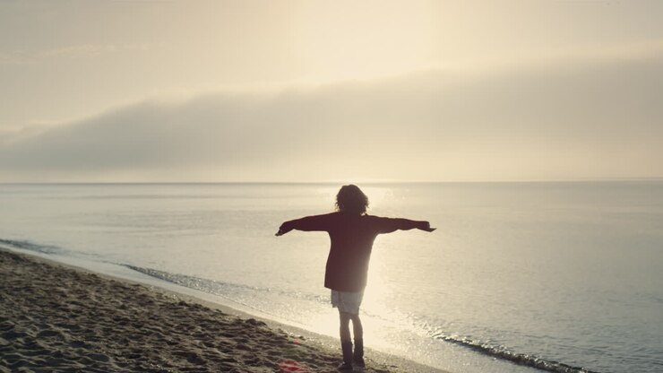 Garota feliz passando férias na praia ao nascer do sol. Mulher positiva levantando as mãos.