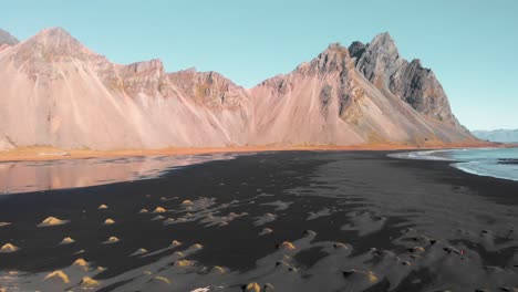 coches en un camino de tierra a lo largo de la playa de arena negra debajo de la montaña vestrahorn