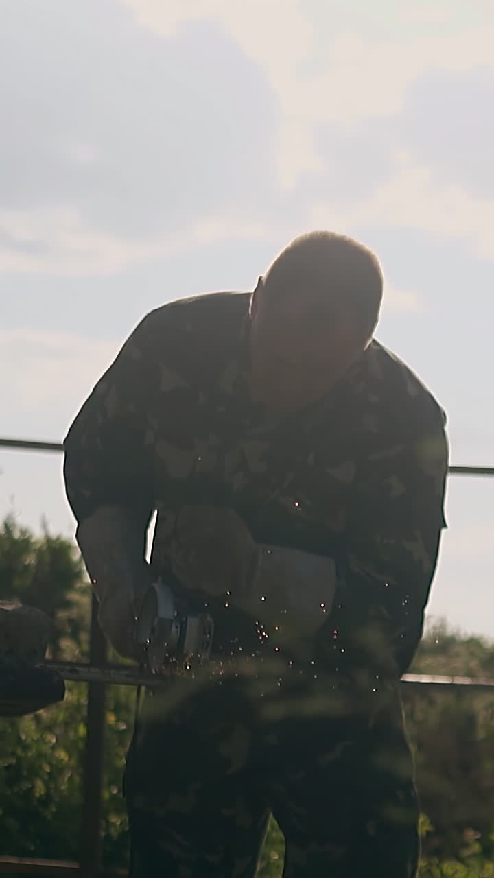strong man cuts details for fence on table using hand disc saw at sun backlight in green yard