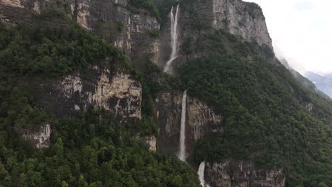 aerial view captures the majestic seerenbachfälle waterfall as it cascades down a steep, forested cliff and into the walensee, switzerland. the panoramic scene highlights the alpine landscape