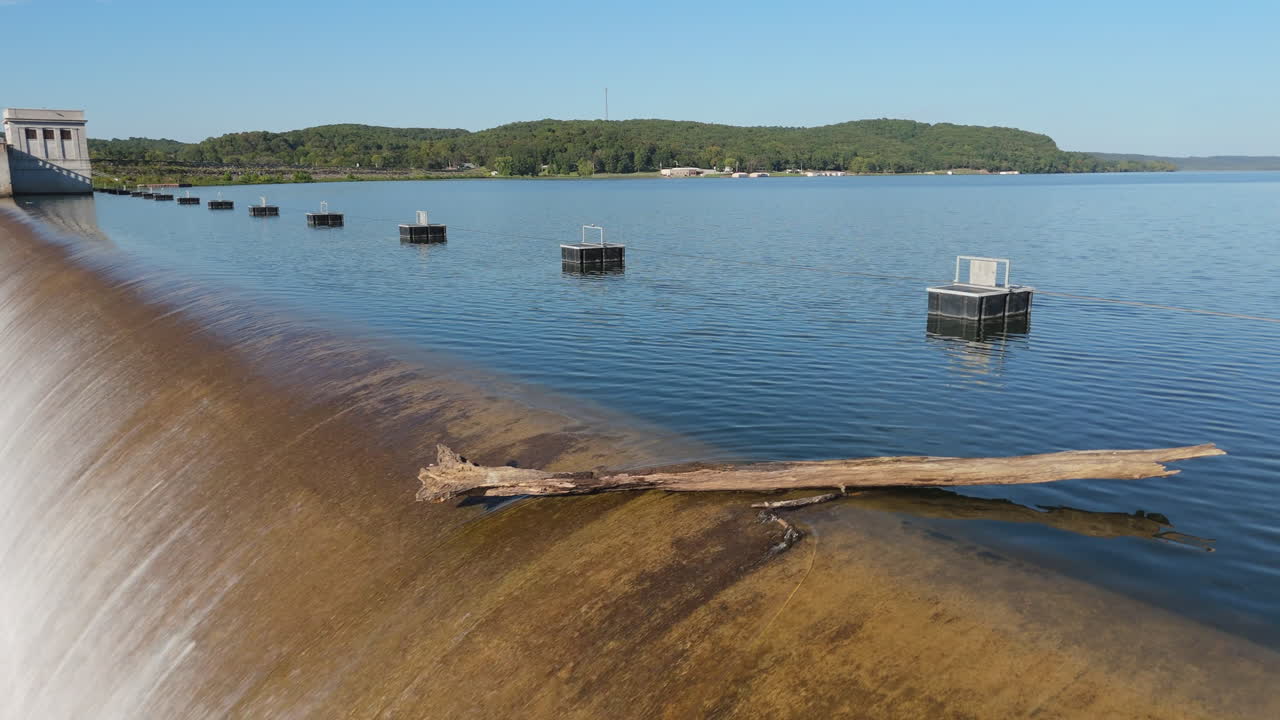 Spavinaw Spillway water crest flowing over concrete curve in Oklahoma, USA, aerial closeup of log balanced