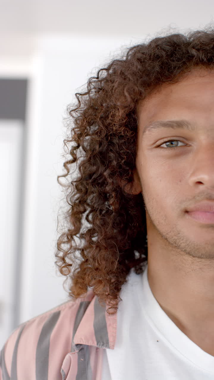Vídeo vertical: Um jovem birracial com cabelo castanho encaracolado olha para a frente