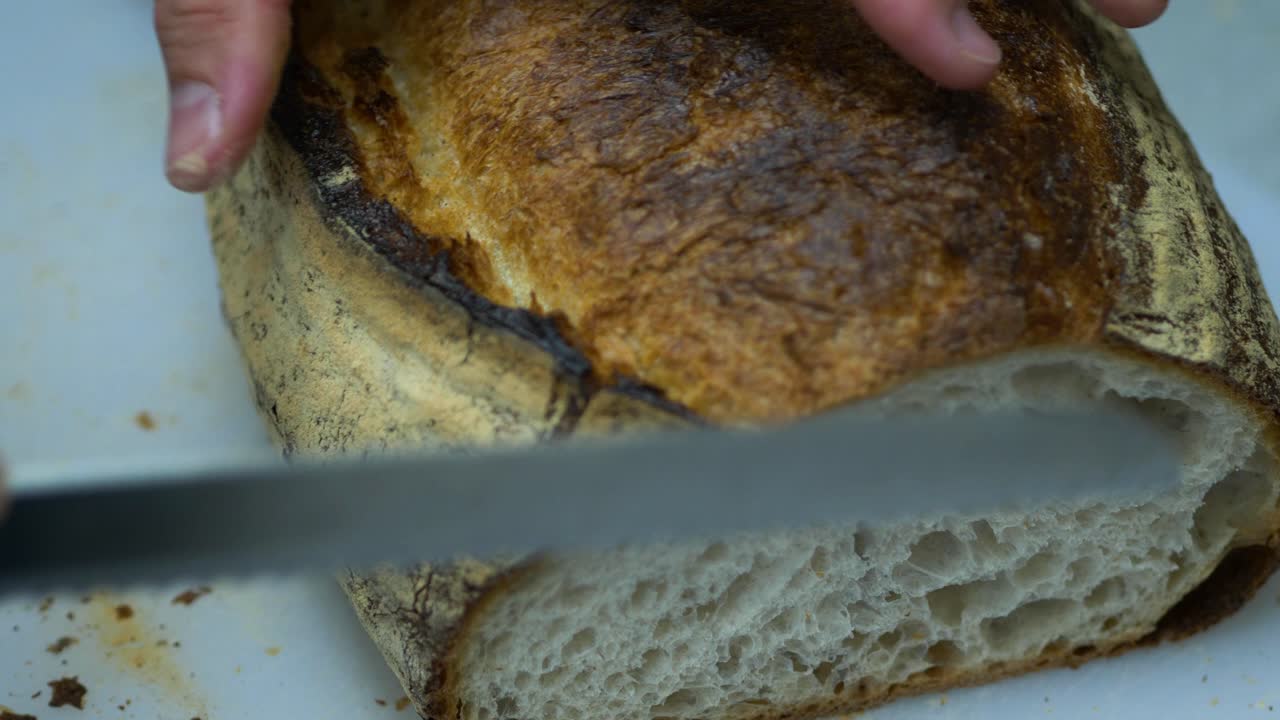 Chef slicing fresh sourdough loaf in cafe kitchen, closeup