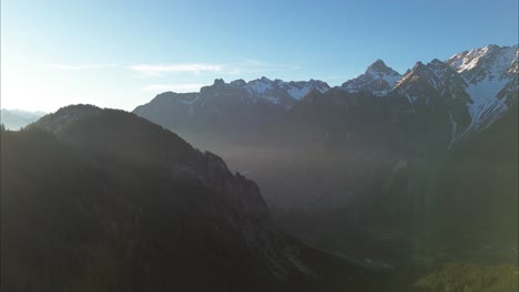 Aerial-Drone-Flight-towards-Sun,-above-Beautiful-Mountain-Landscape-surrounded-by-Forest