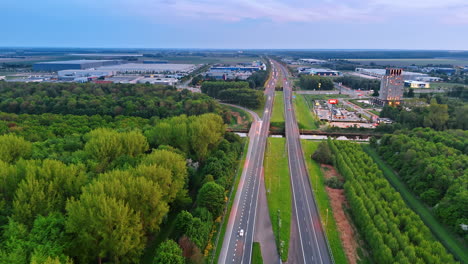 winding road through lush landscape. aerial view captures a highway winding between vibrant green forests and open fields near urban development at dusk
