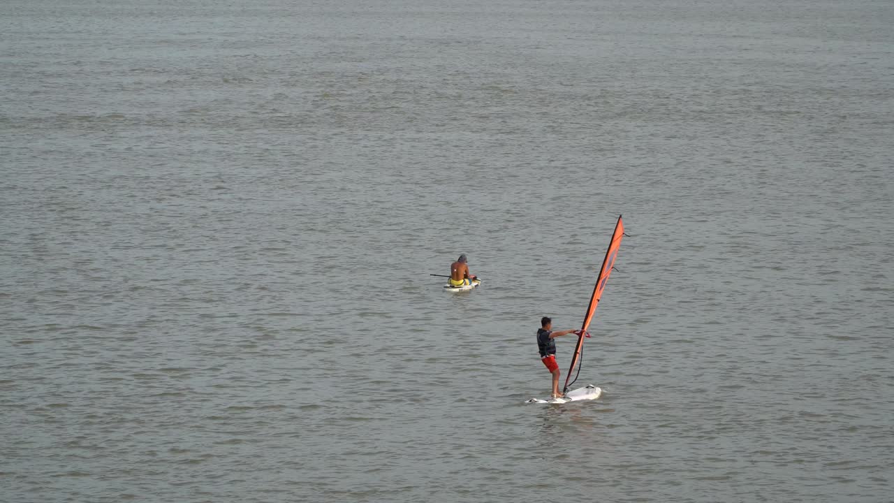 chico haciendo windsurf en el río han con un hombre sentado en una tabla de surf en el fondo