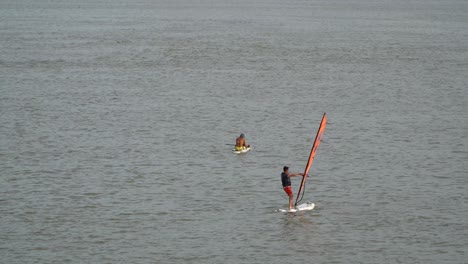 chico haciendo windsurf en el río han con un hombre sentado en una tabla de surf en el fondo