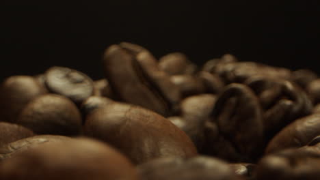 close camera movement through falling fresh coffee beans into a pile of beans laying on a wooden surface