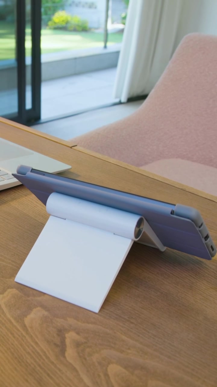 Vertical video: Panning camera showing tablet in blue case on white stand at desk, yard visible