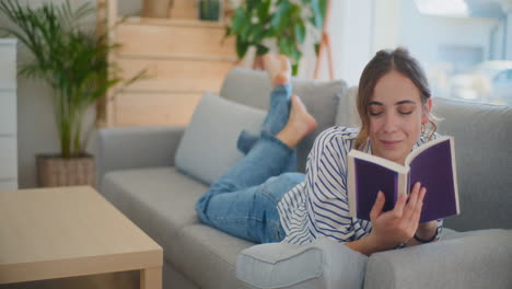 mujer sonriente leyendo su libro favorito en el sofá