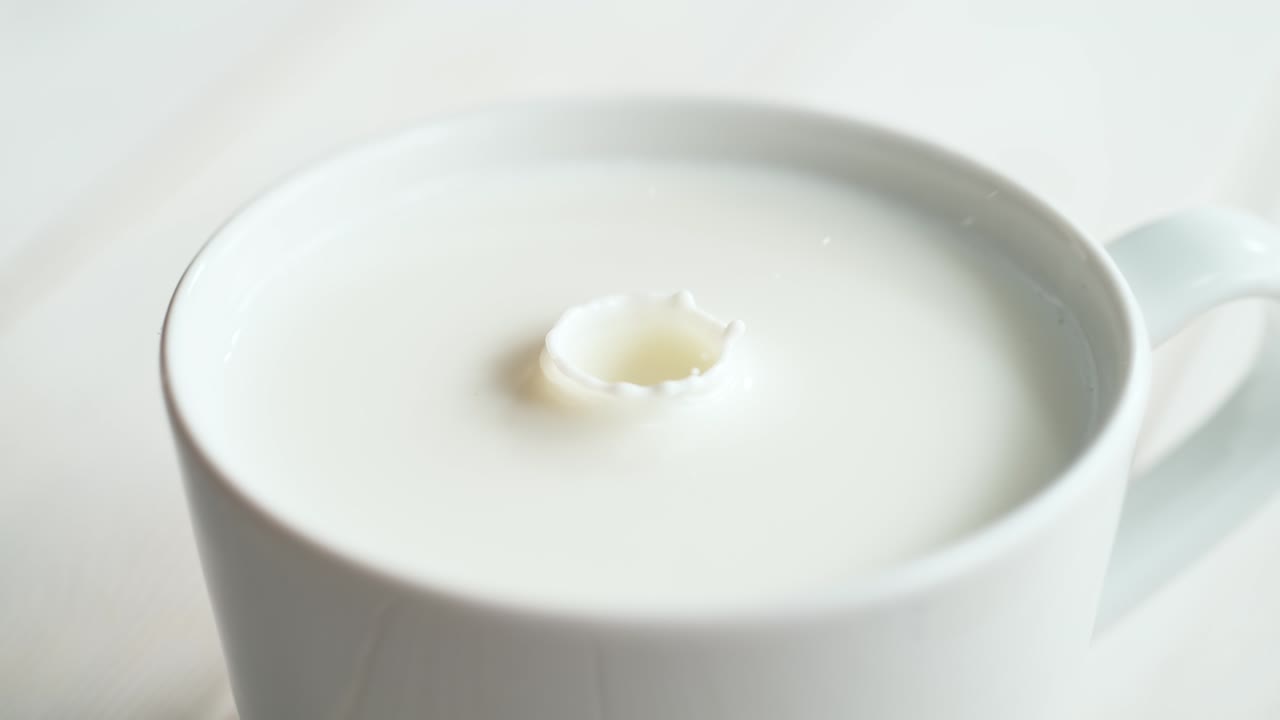 밝은 배경 에 크림 같은 액체 가 있는 컵 에 떨어지는 우유 방울