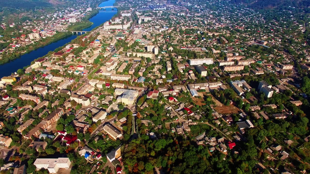 Densely built city landscape with lush greenery. Sunny view of the city on the river banks. Aerial view.