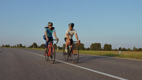 front view of a young couple or friends riding their bikes in the city park or boulevard in summertime. people leisure and lifestyle concept