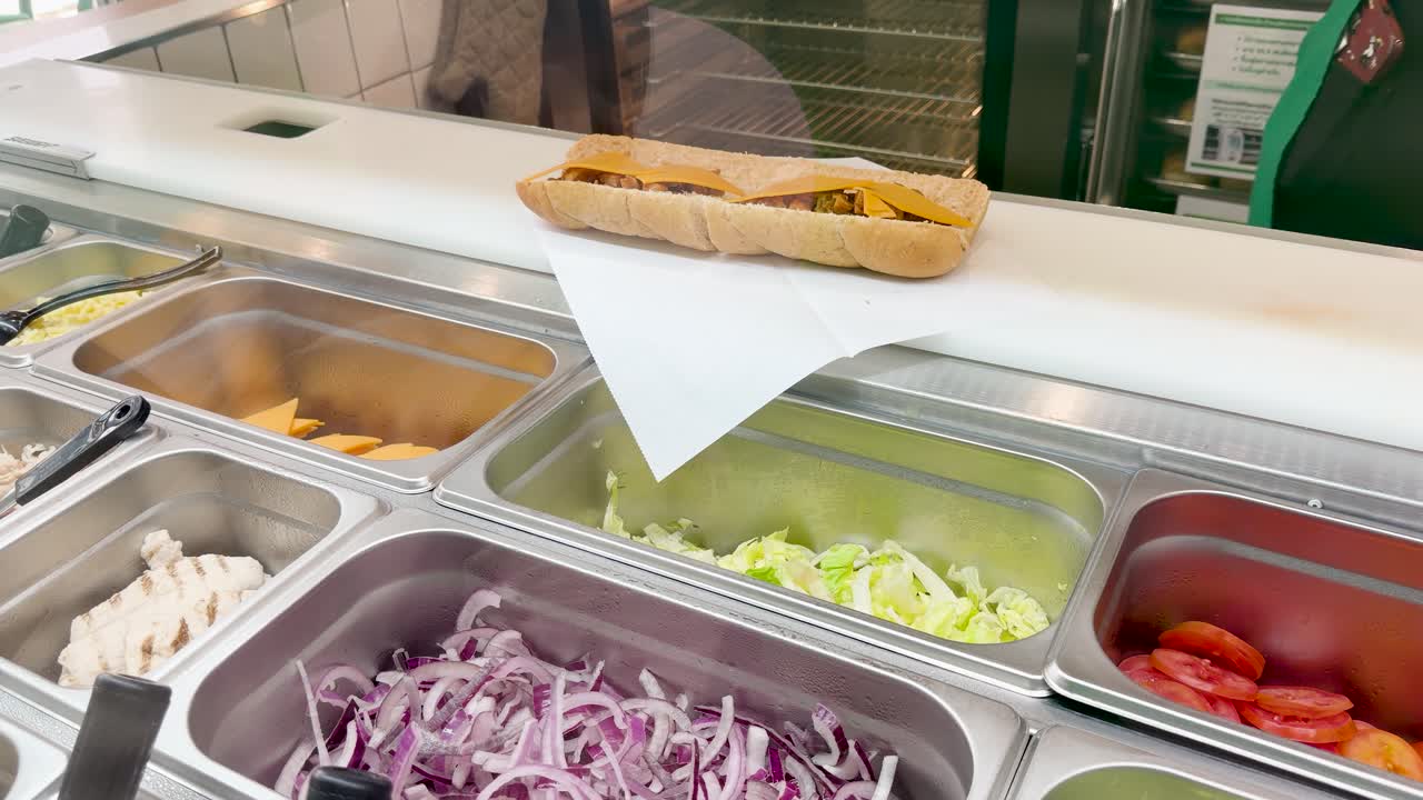 Un lavoratore guantato assembla un panino sub con carne e formaggio nella cucina di un ristorante