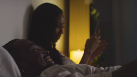 Couple-With-Relationship-Problems-Arguing-At-Home-At-Night-With-Woman-Looking-At-Mobile-Phone-In-Bedroom-1