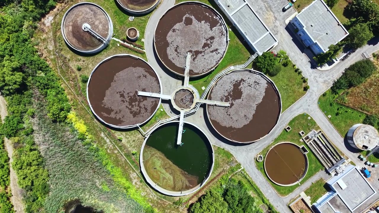 Una planta de tratamiento de agua opera en una zona urbana con múltiples tanques redondos para el procesamiento de aguas residuales durante el día.