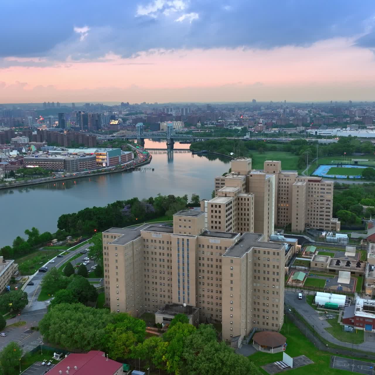 Smooth surface of the river flowing in New York. Busy multi-lane highway with numerous moving cars. Cityscape at sun down
