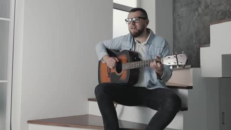 músico masculino cantando y tocando la guitarra en casa