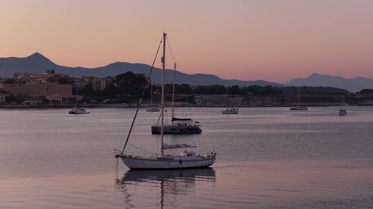 Tramonto pacifico sul porto della città di Corfù con barche a vela ancorate e montagne lontane in Grecia