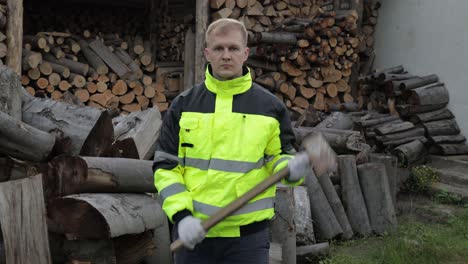 Lumberjack-in-reflective-jacket.-Man-woodcutter-hold-huge-axe-show-ok-sign.-Sawn-logs,-firewood