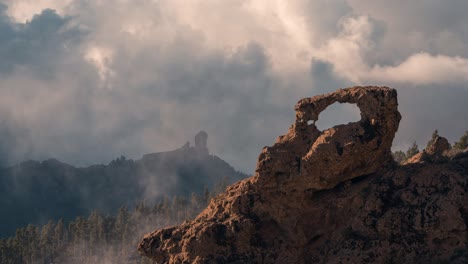 Breathtaking timelapse of Roque Nublo and ventana Ganifa at sunset, with golden light over the mountains and Teide in the distance cloudy day.
