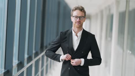 Waist-up-portrait-of-a-business-man-with-glasses-standing-in-a-glass-corridor