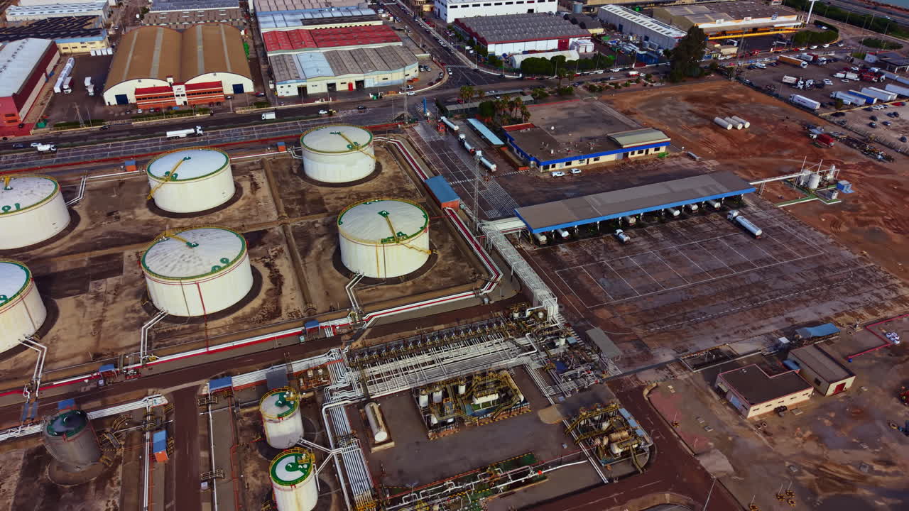 Grandes tanques de almacenamiento de petróleo y zona industrial en una ciudad concurrida en un día soleado, con vehículos y edificios al fondo.