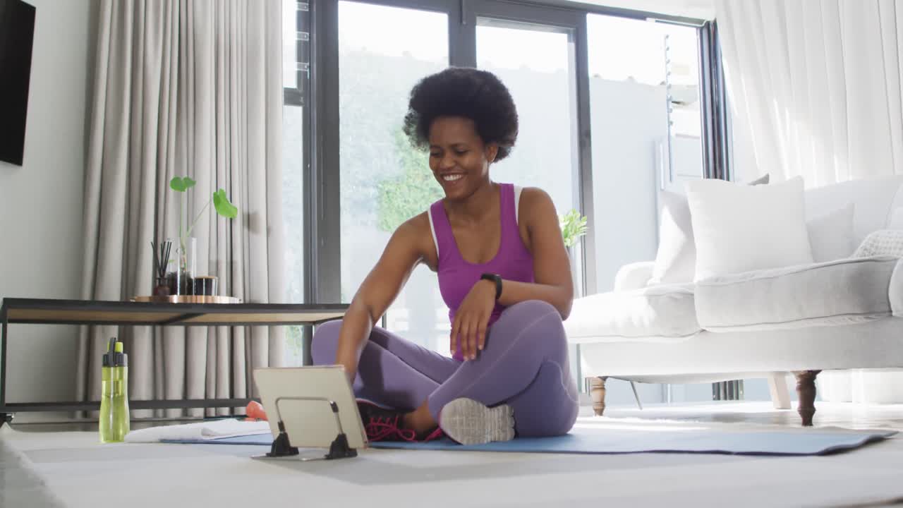 Donna afroamericana felice in abbigliamento sportivo, che si allena e usa un tablet.