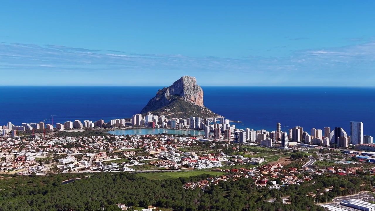 Veduta panoramica di Calpe, Spagna, che mostra l'iconica formazione rocciosa del Peñón de Ifach che si erge sopra la città costiera con il Mar Mediterraneo sullo sfondo.