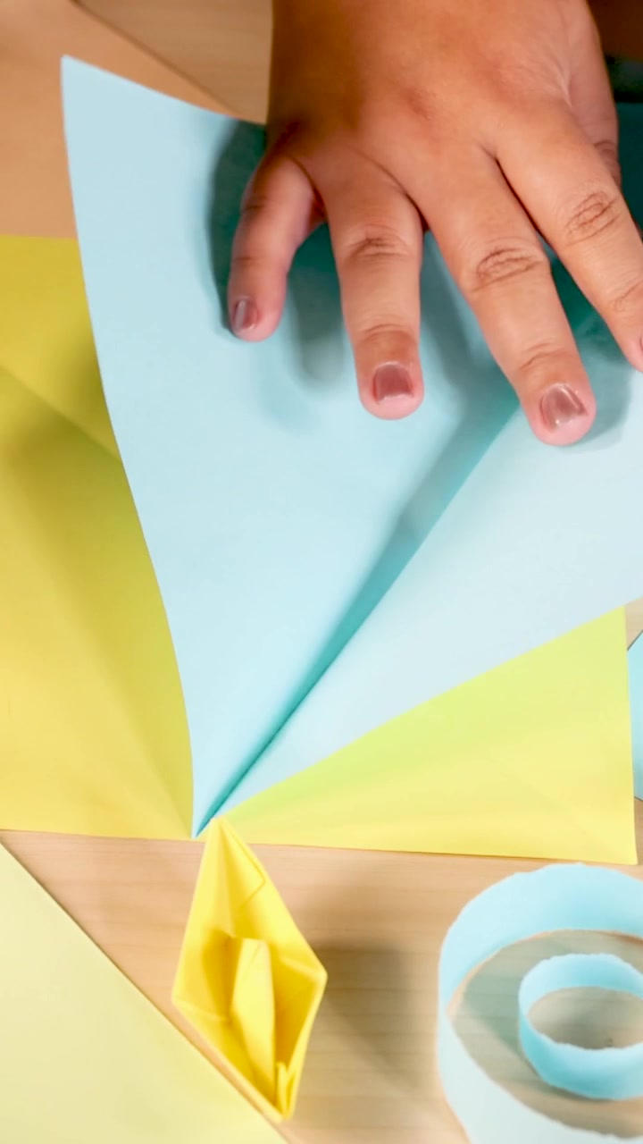 Un'inquadratura verticale dettagliata di mani che piegano con cura carta blu e gialla su legno.