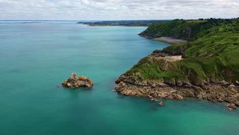 drone shot over gwin zégal bay. the drone flies forward above turquoise water and green cliffs.