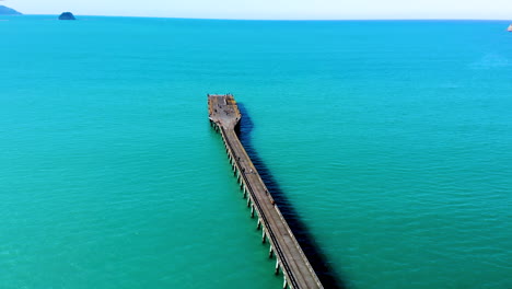 People-walking-on-Tolaga-Bay-Wharf,-aerial-Pacific-Ocean-reveal