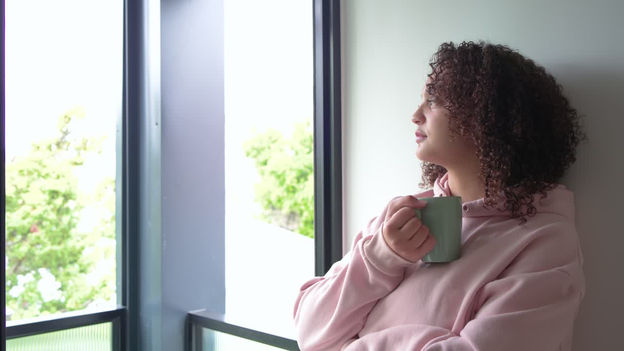 Donna alla porta aperta del balcone, che tiene una tazza, sorseggia, si appoggia, cercando calma, indossando una felpa con cappuccio, con spazio per il testo