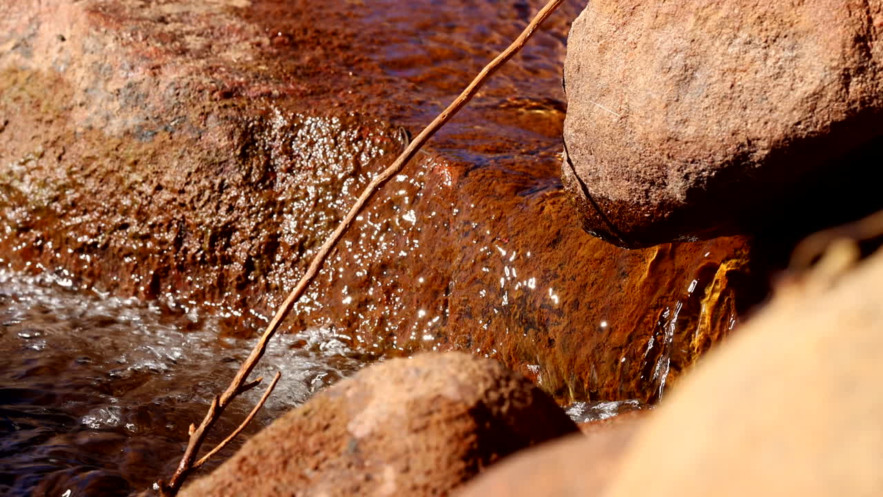 Fresh water stream flows peacefully over iron rich red rocks, telephoto
