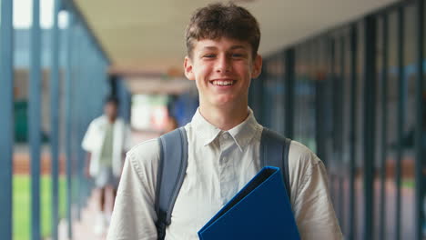 portrait of smiling male high school or secondary student with backpack outside classroom