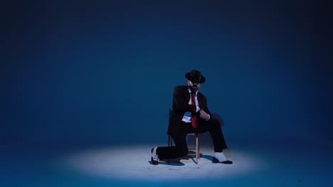 a man in a suit and hat posing on a chair under a spotlight