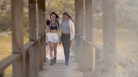 two athletic woman hikers walk along wooden bridge, wind blows hair