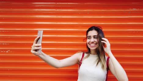 slow motion:beautiful young girl takes selfie with smartphone in front of orange,red background