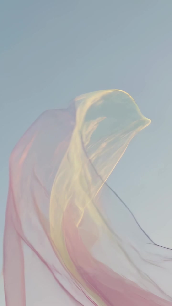 Vidéo verticale : Tissu translucide flottant se transformant dans le ciel bleu sous l'effet d'un léger vent, montrant des teintes pastel.