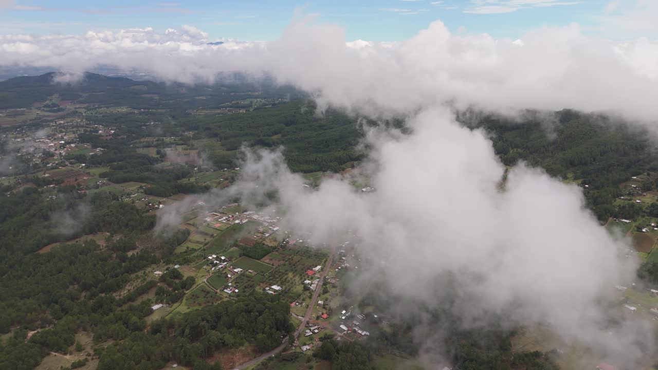 High above the sky, clouds drift over green forests and scattered villages, offering a peaceful view of nature and rural life.