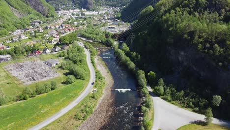 Dale-salmon-river-with-Dalekvam-town-centre-and-BKK-hydroelectric-powerplant---High-voltage-power-cables-crossing-in-front-of-camera---River-coming-straight-from-powerplant---Aerial-Norway