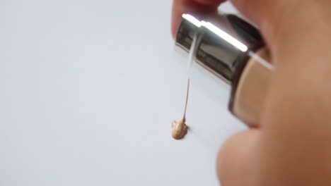 close-up of an individual squeezing a pea-sized amount of liquid foundation on a clean, white board