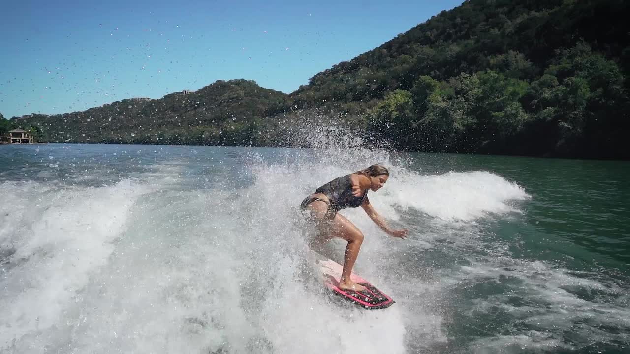 Female wake surfer landing big air grab in slow motion while wake surfing on Lake, Austin Texas