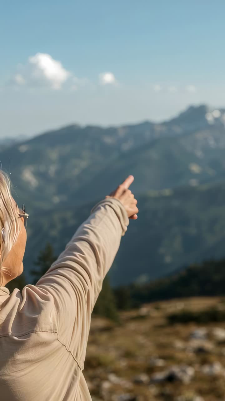 Vertical video: Seeing peak at ridge, hiker in beige top, glasses pointing toward peaks, copy space