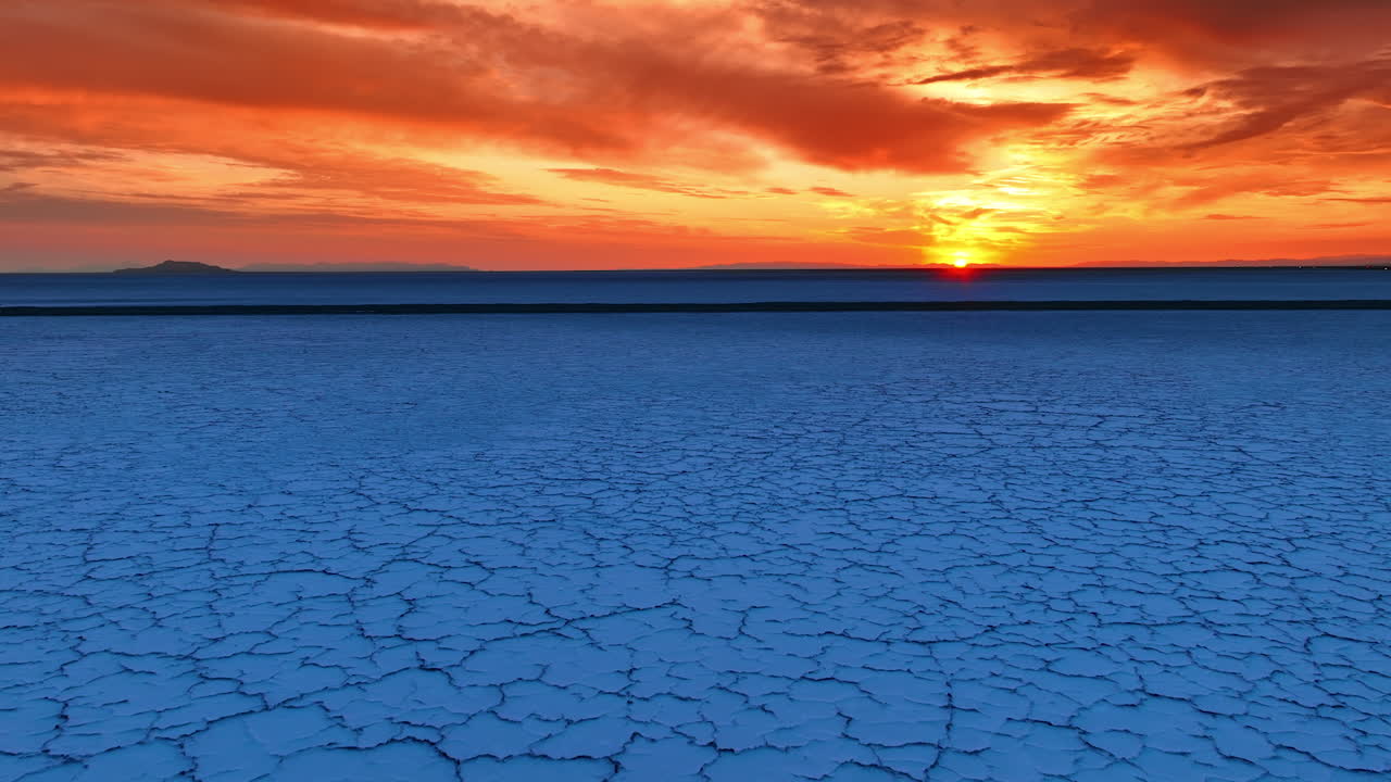 Flight over the cracked salty landscape of Bonneville Salt Flats, Utah, United States. Sun set over the horizon and coloring the sky in orange