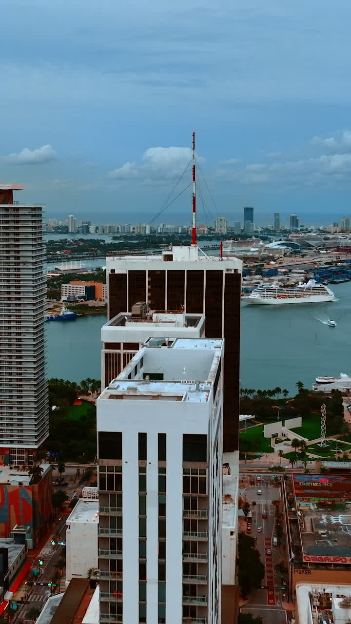 Drone footage among the high-rise buildings and approaching the waterscape. View on Miami, Florida, USA on gloomy day. Vertical video