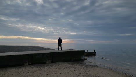 man stood at jetty end at sunset with reveal of coastline of fleetwood beach lancashire uk