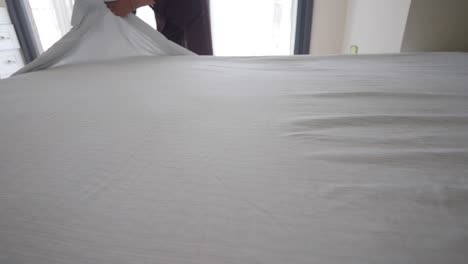 person making a bed and tidying sheets
