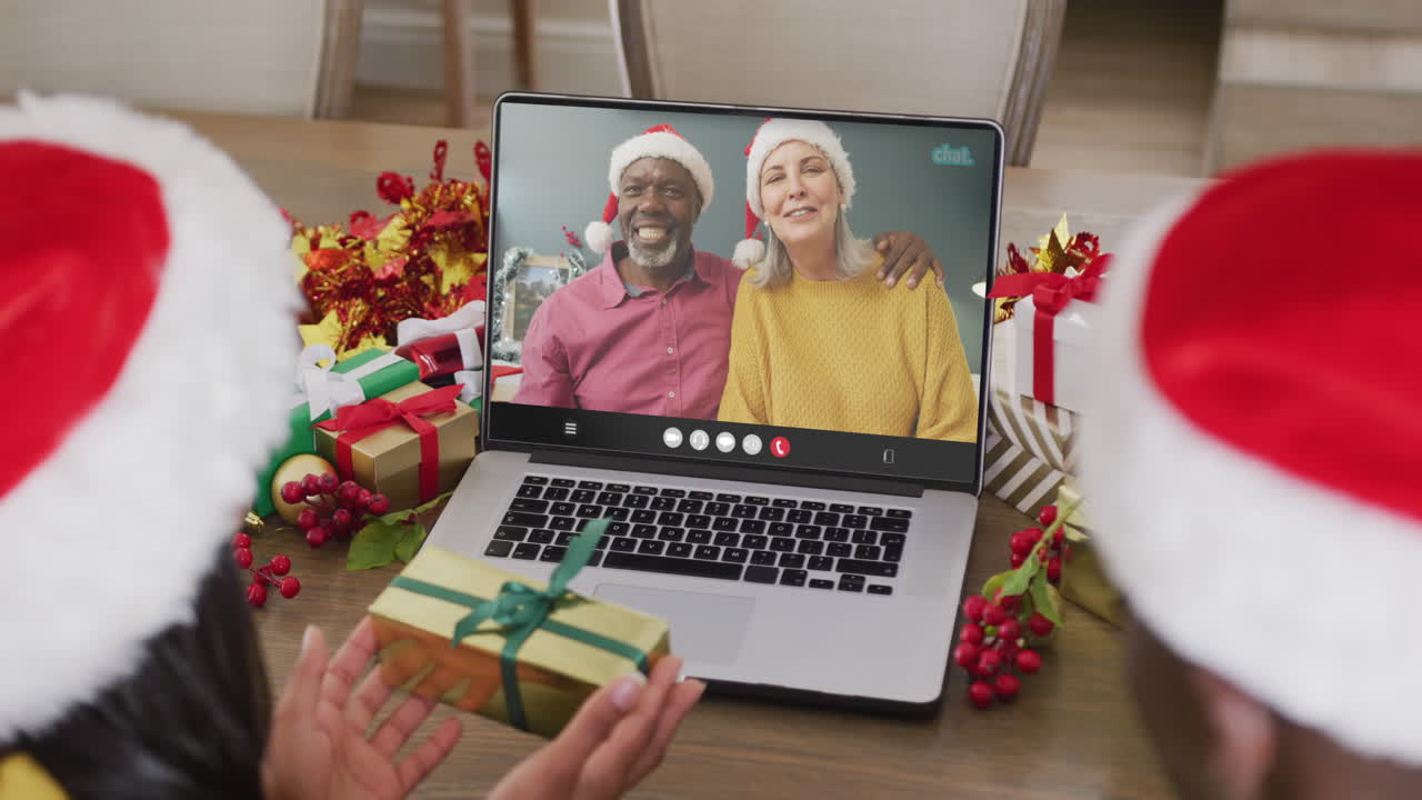 pareja diversa con sombreros de santa teniendo llamada de video portátil con pareja diversa