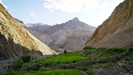 tilt up shot in a hidden, lush green valley between harsh, high mountains day time